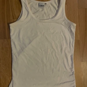 Vit linnetopp från Cubus - En klassisk vit linnetopp från Cubus i enkel och stilren design. Toppen är ärmlös med rund halsringning och tillverkad i mjuk bomull, perfekt för att matcha med jeans eller shorts. Snygg och basic för alla tillfällen.