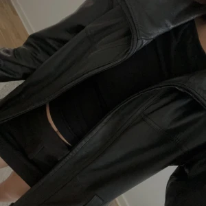 Svart skinnjacka från Wilsons Leather - Säljer en svart skinnjacka från Wilsons Leather i klassisk modell med snygg krage och raka linjer. Jackan har långa ärmar, två fickor framtill och en vinröd insida. Perfekt för dig som gillar stilren och tidlös look.