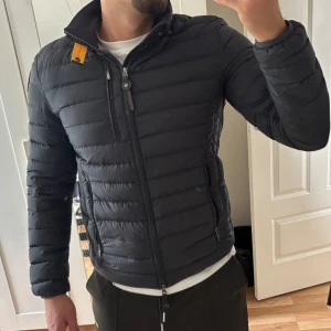 Svart pufferjacka från Parajumpers - Säljer en svart pufferjacka från Parajumpers med klassisk patch på ärmen och gul detalj vid kragen. Jackan har dragkedja framtill och två sidofickor med dragkedja. Använd ett fåtal gånger, kommer i mycket bra skick. 