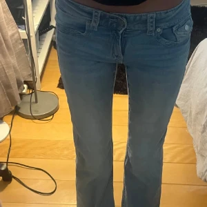 Blå bootcut jeans med låg midja - Säljer ett par snygga blå jeans med bootcut passform och låg midja. Jeansen har klassisk femficksdesign, knapp och dragkedja framtill men också fickor baktill. Perfekta för dig som gillar en avslappnad och trendig stil. Materialet är jeans och färgen är ljusblå. (Modellen säljs inte längre i butik eller hemsida)