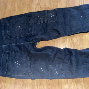 Svarta cargopants med vita prickar S - Svarta cargopants från Zara i storlek S med coola vita prickdetaljer och stora fickor på benen. Byxorna har en loose passform och är tillverkade av en mix av bomull och polyester med lite elastan för extra komfort. Perfekt för dig som gillar streetstyle och vill sticka ut.