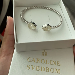 Silverfärgat armband Caroline Svedbom - Snyggt armband i silverfärg från Caroline Svedbom med tvinnad design och två stora, klara kristaller i ändarna. Använd få tal gånger! 🤍