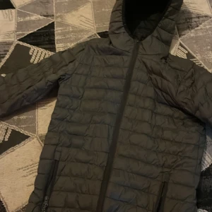 Svart pufferjacka från Neomondo - Svart pufferjacka från Neomondo med huva och hel dragkedja framtill. Jackan är quiltad och har två fickor med dragkedja. Perfekt för kyliga dagar och har en clean, sportig look som funkar till det mesta.