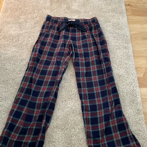 rutiga pyjamasbyxor från gina tricot med rosett vid midjan - Snygga rutiga byxor från Gina Tricot i blått, rött och grönt. De har en bred resår i midjan och en dekorativ rosett framtill. Byxorna är raka i modellen och tillverkade i mjukt bomullstyg, perfekta för en chill och trendig look.