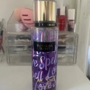 Victoria's Secret Love Spell mist - Fräsch och söt body mist från Victoria's Secret i doften Love Spell. Flaskan är lila med holografisk text och har ett elegant guldigt lock. Perfekt för dig som gillar fruktiga och blommiga dofter. Snygg design som passar på sminkbordet.