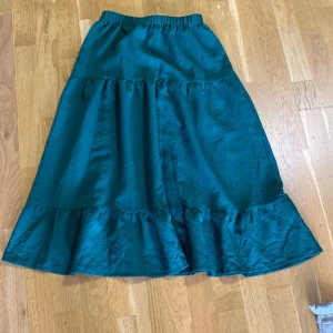 Grön  långkjol med volang - Snygg grön  långkjol med bred resår i midjan och volangdetaljer nertill. Kjolen har en flowy känsla och är perfekt för dig som gillar en avslappnad men ändå trendig stil. Materialet känns mjukt och lätt, vilket gör den superbekväm att bära.