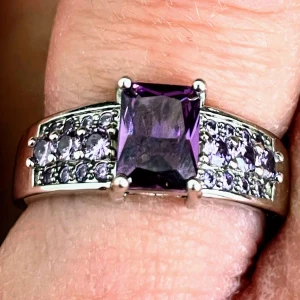 Silverring med lila stenar - Snygg silverring med en stor, fyrkantig  ametist i mitten och mindre lila stenar på sidorna. Ringen har en elegant och glittrig design som verkligen drar blickarna till sig. Äkta S925 silver