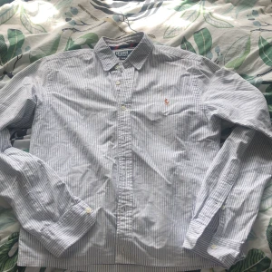 Randig Ralph lauren skjorta - Säljer en riktigt fet Ralph lauren skjorta i blåvitt randigt med en skitsnygg färgad ralph lauren icon, perfekt för varmare väder. Skjortan har en mindre slitning i kragen som syns på bild fyra men inte är synlig alls vilket du ser på bild fem och det är därför priset är så lågt. Passar någon kring en och sjuttio. Skicka meddelande kring mista fundering