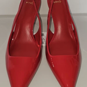 Röda pumps med spetsig tå från MNG - Helt nya. Säljes pga ej kommer till användning. Snygga röda pumps från MNG med glansig finish och spetsig tå. Skorna har öppen häl med smal rem och elegant klack. Kontakta mig för fler frågor. Priset kan diskuteras vid snabb affär.