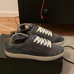  Intressekoll!!! Saint Laurent blå sneakers  - Snygga blå sneakers från Saint Laurent i mocka med vit sula och vita snören. Diskret logga på sidan och på plösen. Skorna har en klassisk låg profil och rund tå, perfekt för en stilren och trendig look. Skorna är lite slitna på sulan men inget som man tänker på. Går också med på byten av skor helst flycrew eller lv. Dustbag och box osv finns. Bara att fråga på om de är något speciellt ni undrar över. Mvh Oscar ✌🏼☺️