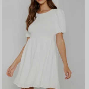 Vit kort klänning med puffärm - Supersöt vit kortklänning med puffärmar och smockad överdel. Klänningen har öppen rygg med knytband upptill och en flowy kjol. Perfekt för student, skolavslutning, midsommar och andra tillfällen, ger en fräsch och trendig look.