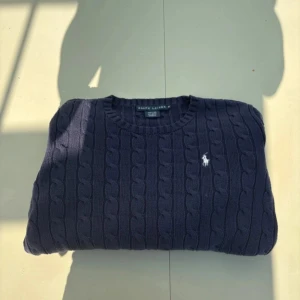 Mörkblå kabelstickad tröja Ralph Lauren - Kabelstickad mörkblå tröja från Ralph Lauren i 100% bomull. Klassisk rund halsringning och långärmad modell med broderad vit logga på bröstet. Perfekt för dig som gillar preppy och stilren look. Pris går att diskuteras.