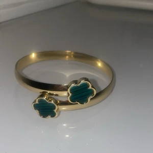 Guldigt armband & örhängen med gröna blommor - Snyggt set med armband och örhängen i guldton med gröna blommor i fyrklöverform. Blommorna har en randig effekt i det gröna och ger en cool, unik look. Perfekt för dig som vill sticka ut med detaljer som känns både trendiga och klassiska. Aldrig använda. 🌸