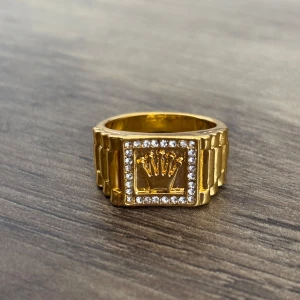 Guldfärgad ring med kristaller - Snygg guldfärgad ring med en fyrkantig design och glittrande kristaller runt en central detalj. Perfekt för att ge en lyxig touch till din stil.