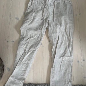 Beiga linnebyxor från Dressmann L - Snygga och luftiga beiga linnebyxor från Dressmann i storlek L. Byxorna har resår i midjan med snörning och sidfickor, perfekta för varma dagar. Materialet är en skön linneblandning som ger en avslappnad vibe.