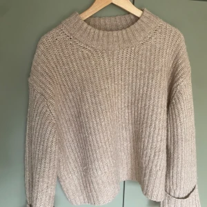 Jätte snygg Beige stickad tröja från Gina Tricot - Mysig beige stickad tröja från Gina Tricot med grov ribbstickning och bred krage. Perfekt till en sval sommarkväll, med en vit långkjol. Tröjan har en relaxed passform och långa ärmar, perfekt för lager på lager under kyliga dagar. Enkel att matcha med jeans eller kjol för en chill look.