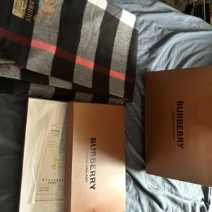Rutig kashmirhalsduk från Burberry - Exklusiv halsduk från Burberry i 100% kashmir. Klassisk rutig design i svart, grått, vitt och rött med broderad Burberry-logga och ryttare. Kommer med originalförpackning och Burberry-påse. Perfekt accessoar för att lyfta din stil.