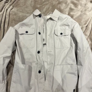 Beige overshirt  - Stilren beige overshirt från H&M med klassisk krage, stora bröstfickor med knappar och två sidofickor. Jackan är tillverkad i bomull och har långa ärmar samt knäppning framtill. Perfekt för lager-på-lager och enkel att matcha. Sparsamt använd, inga defekter mitt pris 175