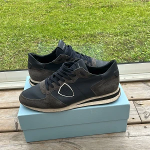 Philippe Model TRPX - Snygga sneakers från Philippe Model i mörkblått och grått. Ovandel i en mix av mocka och skinn med vita detaljer och klassisk snörning. Skorna har en platt sula och rund tå, perfekt för en stilren och sportig look. Allt og medföljer,