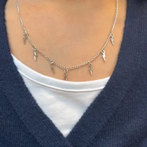 Silverhalsband med blixtberlocker - Snyggt halsband i silverfärgad metall med små blixtformade berlocker längs kedjan. Kedjan är tunn och smidig, och blixtarna ger ett coolt och edgy intryck. Perfekt för dig som vill sticka ut med en unik detalj.