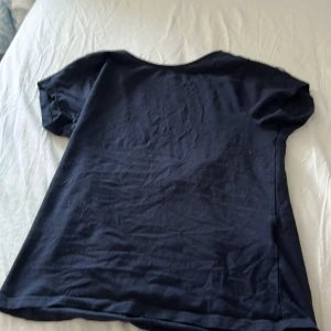 Mörkblå topp från Gina Tricot - En basic mörkblå topp från Gina Tricot med rundad, djup urringning framtill och korta ärmar. Tillverkad i mjuk bomull, perfekt för en enkel och clean look. Passar dig som gillar stilrena plagg med avslappnad vibe.