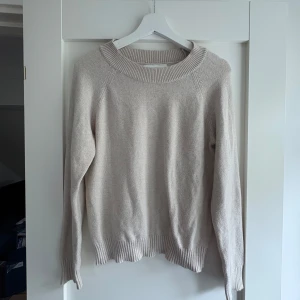 Beige stickad tröja med rund hals - En stilren beige stickad tröja med rund halsringning och ribbade muddar. Tröjan har en avslappnad passform och är perfekt för lager-på-lager. Passar dig som gillar en enkel och clean look.