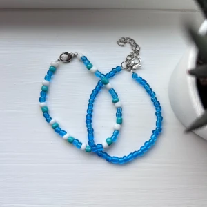 Blått och vitt pärlarmband - Två handgjorda armband med små glaspärlor i blått, vitt och turkost. Ena armbandet är helblått medan det andra har ett mönster av blå, vita och turkosa pärlor. Båda har silverfärgat lås och justerbar kedja. Perfekt accessoar för en färgglad look. Hemmagjorda. Önskar du veta exakta mått? Tveka inte att höra av dig!
