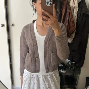 Brun kofta från Enkel Studio - Mysig brun kofta från Enkel Studio med två stora fickor framtill och snygga knappar. Koftan är stickad och har en croppad passform med långa ärmar och ribbade muddar. Perfekt att slänga över en t-shirt eller klänning för en chill look. Lite nopprig annars i fint skick❤️