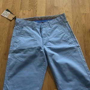 Ljusblå chinos från Pitbull, W29 - Snygga ljusblå chinos från Pitbull med klassisk passform och coolt mönstrat innerfoder. Byxorna har bälteshällor, snedställda fickor fram och två bakfickor med knapp. Perfekta för dig som vill ha en fräsch och stilren look.