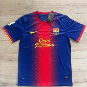 FC Barcelona Messi 10 Nike matchtröja - Säljer en officiell FC Barcelona matchtröja från Nike med Messi 10-tryck. Tröjan är blå och röd med gula detaljer, klubbmärke på bröstet och Qatar Foundation-tryck. Tillverkad i lätt och ventilerande Dri-FIT polyester. Korta ärmar och rund hals.