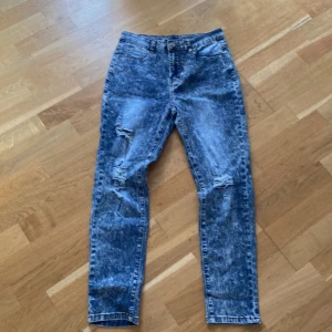 Acid wash blå jeans med slitningar - Säljer ett par blå acid wash jeans med snygga slitningar på knäna. Jeansen har hög midja och raka ben, klassisk femficksmodell och stängs med dragkedja och knapp. Perfekta för en cool och avslappnad stil.
