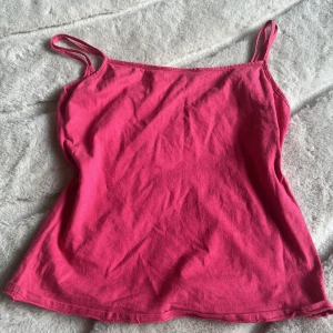 Rosa linnetopp med smala axelband - Enkel och snygg rosa linnetopp med smala axelband. Toppen har rak passform och är tillverkad i mjuk bomull, perfekt för varma dagar. Färgen är klar rosa och modellen  är ärmlös för en luftig känsla.