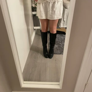 Svarta höga stövlar med klack - Snygga svarta stövlar i skinnimitation med hög, stabil klack och fyrkantig tå. Stövlarna går upp till knäet och har en stilren, minimalistisk design som passar perfekt till kjol eller klänning. Perfekta för dig som vill ha en trendig och klassisk look. Nypris är 899 och dem är helt oanvända💕