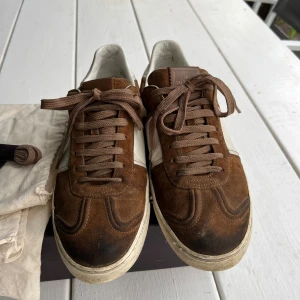 Valentino Garavani bruna sneakers mocka - Snygga sneakers från Valentino Garavani i brunt och vitt med ovandel i mocka och skinn. Skorna har bruna snören, vita detaljer och  sula med kamouflagemönster samt små nitar baktill. Box, påse och nya snören ingår. Saknas ett par nitar, se bild.