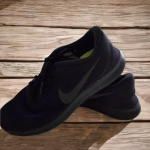 Nike Free RN Flyknit svarta löparskor - Lätta och flexibla Nike-sneakers i svart med ventilerande mesh och mjuk sula. Använda men i gott skick. Perfekta för vardagsbruk eller lätt träning.