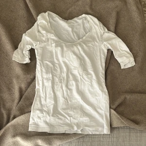 Vit t-shirt med trekvartsärm Filippa K - Vit t-shirt från Filippa K med trekvartsärm och rund, djup urringning. Tillverkad i mjuk bomull som känns skön mot huden. Enkel och clean design som passar perfekt till jeans eller kjol. Snygg basic att ha i garderoben.