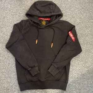 Svart hoodie Alpha Industries S - Svart hoodie från Alpha Industries med stor logga på ryggen. Vid frågor eller funderingar hör av dig!