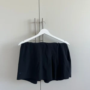 Svart kortkjol från Nike - En svart, stilren kortkjol från Nike med enkel design och lätt utsvängd form. Kjolen är tillverkad i ett mjukt och följsamt material som passar perfekt för en aktiv livsstil. Diskret logga nertill. 