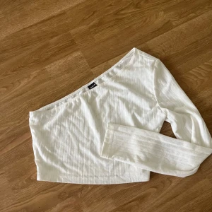 Vit offshoulder topp  - Snygg vit offshoulder topp med lång ärm och diskret ribbad struktur. Toppen har en clean och modern look, perfekt att styla med höga jeans eller kjol. Enkel att matcha och ger en fräsch vibe till din outfit.