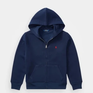 Marinblå hoodie från Polo Ralph Lauren - Säljer en marinblå hoodie från Polo Ralph Lauren i storlek XL. Tröjan har dragkedja, huva och känguruficka framtill. Klassisk röd logga broderad på bröstet. Tillverkad i mjuk bomullsmix med lite polyester för extra komfort. Passar som ett S