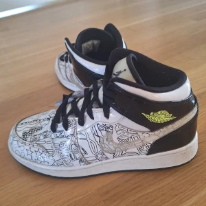 Nike Air Jordans med grafiskt mönster - Snygga Nike Air Jordans med ett unikt grafiskt mönster i svart och vitt. Skorna har svarta snören och en kontrasterande gul detalj vid ankeln. Perfekta för dig som vill sticka ut med en cool stil.