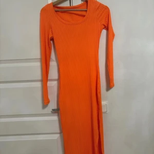 Orange ribbad långklänning - Snygg och iögonfallande orange långklänning med ribbad struktur. Klänningen har långa ärmar och en rund halsringning, perfekt för en färgstark look.
