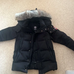 Svart dunjacka från Canada Goose - Säljer en svart dunjacka från Canada Goose med pälskantad huva. Det finns en skada på jackan och det är drag kedjan vid vänstra fickan som e trasig.