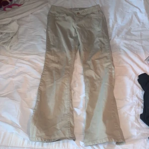 Beige byxor från Lindex - Snygga beige byxor från Lindex med normal passform och raka ben. Byxorna har klassisk design med knappar och dragkedja framtill samt fickor både fram och bak. Perfekta för en stilren look.