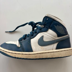 Nike Air Jordans i blått och vitt - Säljer ett par klassiska Nike Air Jordans i blått och vitt. Skorna har snörning och en ikonisk design med perforerade detaljer på tån. Perfekta för dig som älskar sneakers med stil.