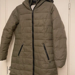 Olivgrön dunjacka från TTDenim - Passar för M. Säljer en olivgrön dunjacka från TTDenim med dragkedja och huva. Jackan har en quiltad design och två fickor med dragkedjor framtill. Perfekt för kyliga dagar.