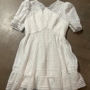 Vit spetsklänning från By Malina - Säljer en vacker vit klänning från By Malina med spetsdetaljer och volanger. Klänningen har korta ärmar och en dragkedja i ryggen. Perfekt för sommaren eller studenten!