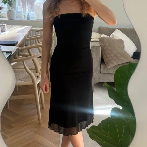 Svart axelbandslös klänning - Snygg svart axelbandslös klänning med en tight passform. Klänningen har en elegant design med en lätt volangdetalj vid fållen. Perfekt för en kväll ute eller en speciell tillställning. Se bilder för skick