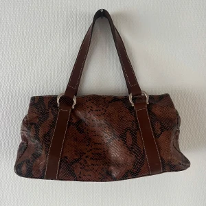 Brun axelväska med ormmönster - Snygg brun axelväska med ormmönster och dubbla handtag. Väskan har en dragkedja och flera fack inuti för enkel organisering. Perfekt för att ge din outfit en trendig touch🤎knappt använd, buda gärna