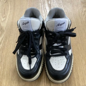 Svartvita sneakers från Axel Arigato - Säljer ett par stilrena svartvita sneakers från Axel Arigato. Skorna har en klassisk design med snörning och en bekväm sula. Perfekta för en casual look.